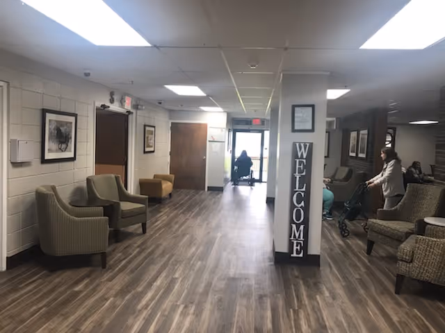 Wide hallway lounge in a senior care facility with chairs along the sides and a pillar displaying a 'WELCOME' sign.