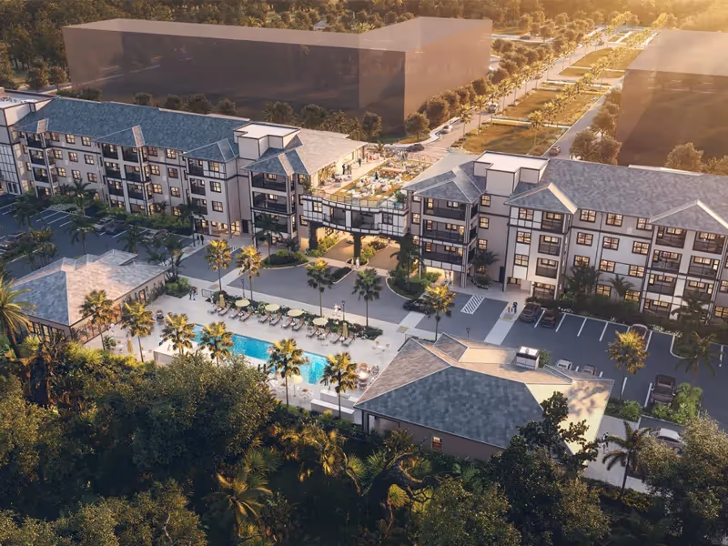 Aerial view of a multi-story senior living complex with connected buildings, a central pool, palm trees, and parking areas.