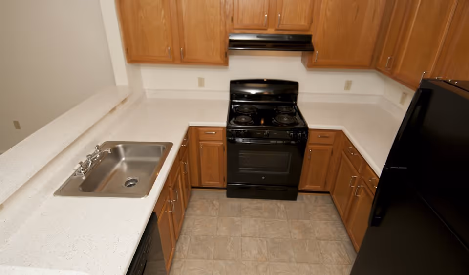 U-shaped kitchen with wooden cabinets, white countertops, a stainless sink, black stove and refrigerator.