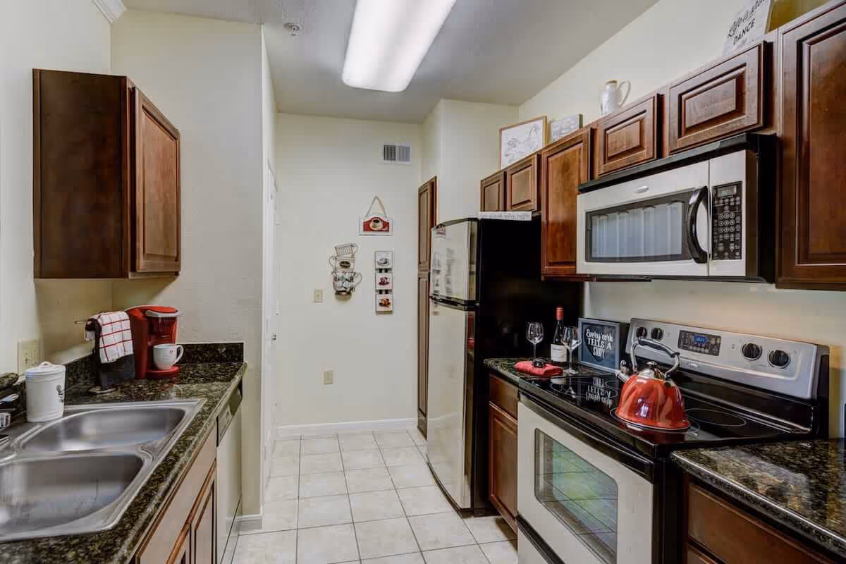 Galley-style kitchen with dark wood cabinets, stainless steel appliances, granite countertops, and a tiled floor.