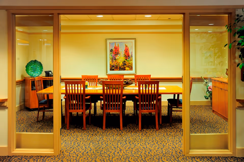 Interior view through glass doors of a dining/meeting room with a long wooden table and several chairs.