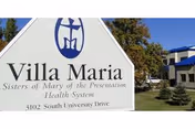 Large white entrance sign reading "Villa Maria" on a lawn with trees and a building visible behind it.