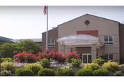 Exterior view of Mcauley Residence building with a covered entrance, landscaped garden with bushes and flowers, and an American flag on a flagpole.