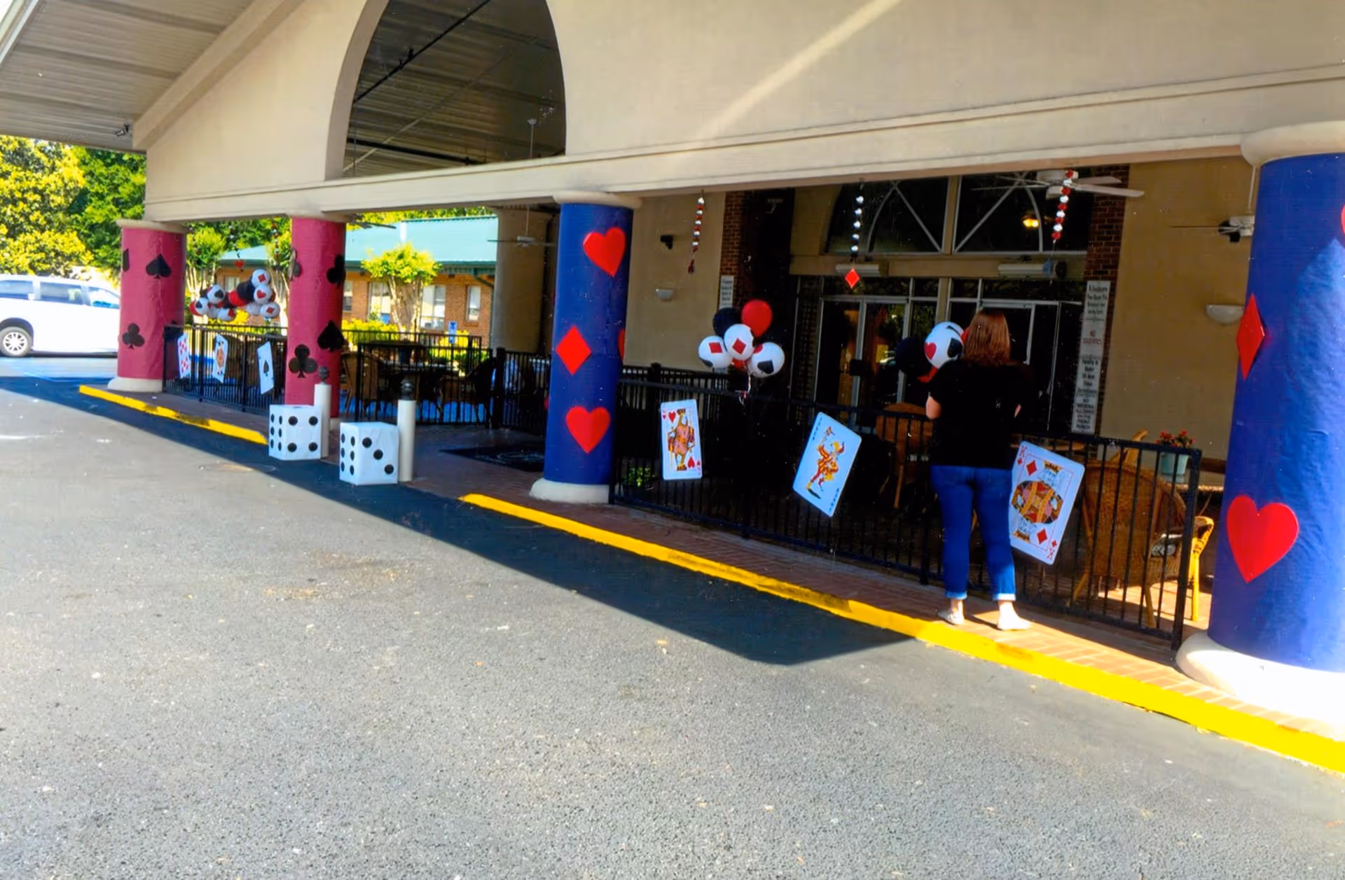 Front entrance of a senior living facility with decorated columns and oversized playing-card and dice decorations, and a person standing near the doorway.