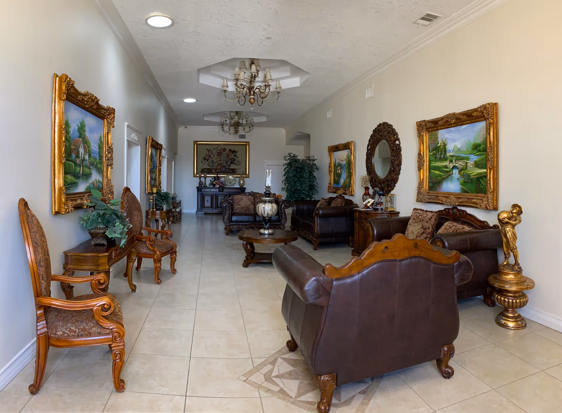 Ornately furnished lounge with leather sofas, wooden chairs, framed landscape paintings, chandeliers and decorative accents along a tiled corridor.