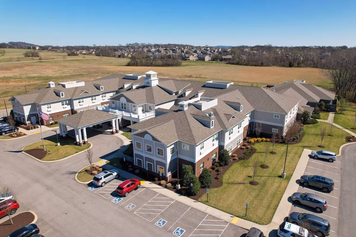 Aerial view of a multi-wing senior living building with an entrance canopy, landscaped lawns, and a parking lot.