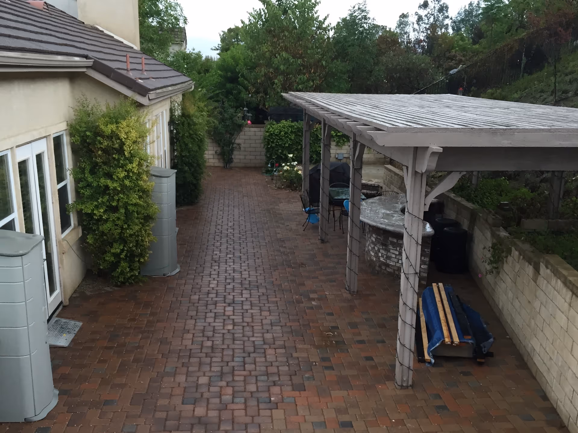 Brick-paved courtyard with a covered seating area and surrounding greenery beside a residence.