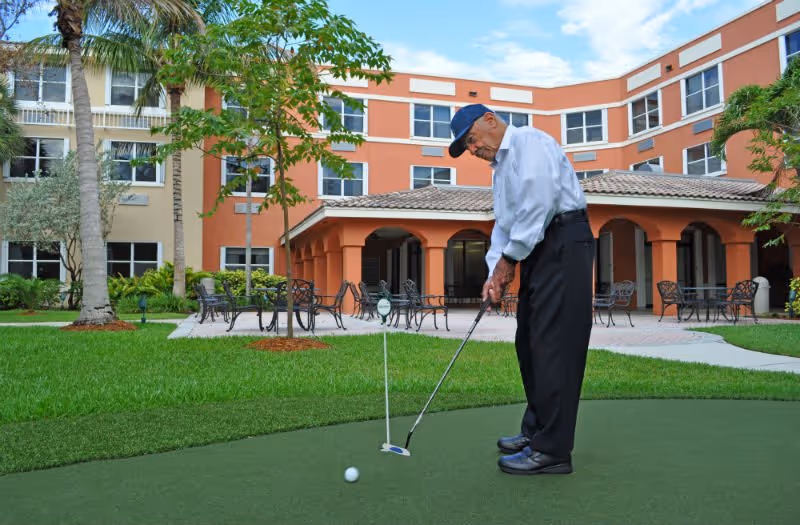 A man putting on a small green in the landscaped courtyard of a multi-story senior living building.