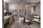 Accessible bathroom with grab bars, a raised toilet, roll-in shower area with a shower chair, sink countertop, and towels.