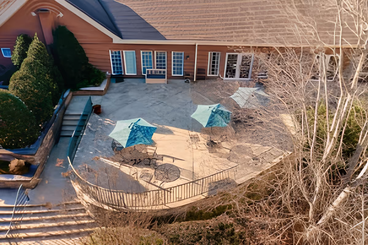 Aerial view of a cracked outdoor patio with blue umbrellas, steps, and a building facade with windows and doors.