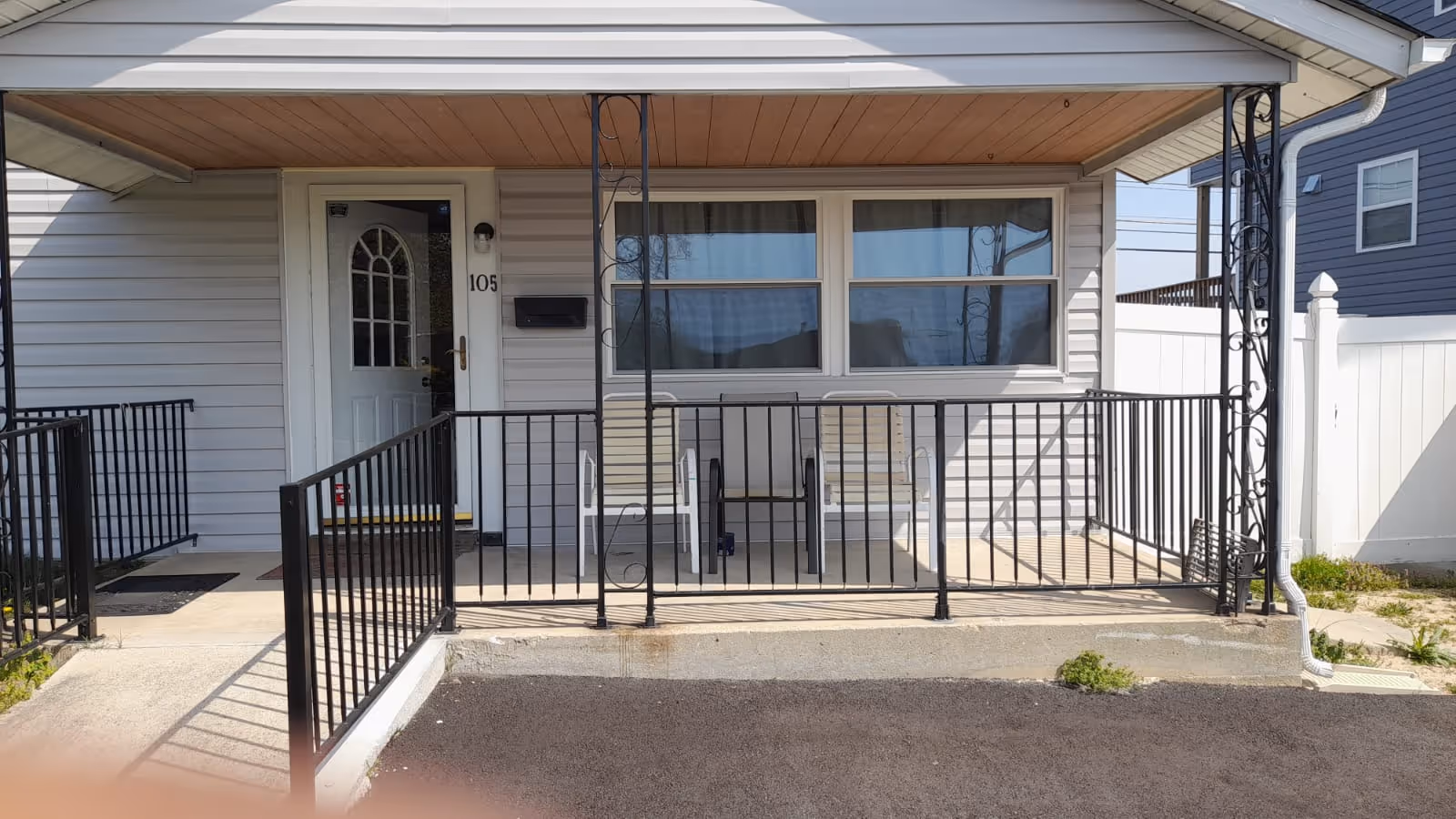 Covered front porch of a single-story unit with a white door numbered 105, black railing and two chairs.