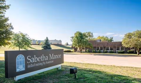 Sabetha Manor exterior signage with the building and surrounding landscaping in view.