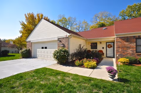 Single-story brick and siding townhouse with a two-car garage, front porch decorated with a fall wreath and potted flowers, and a neatly landscaped lawn and driveway.