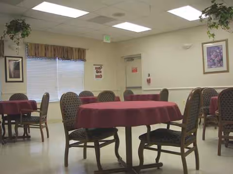 Senior living dining room with round tables, burgundy tablecloths, and padded chairs.