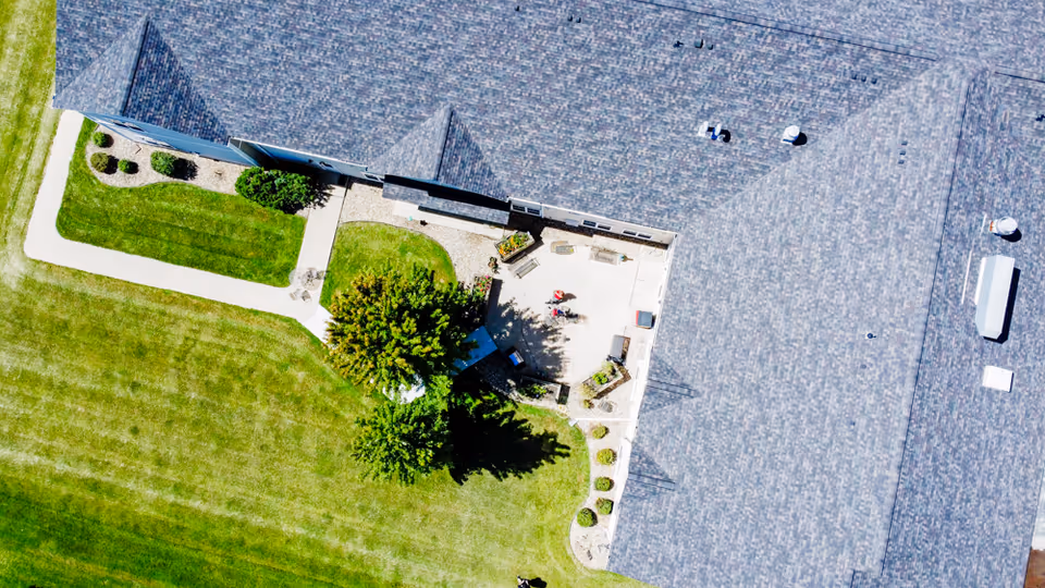Aerial view of a senior living building's rooftop and adjoining courtyard with walkways, lawn, trees, and patio seating.