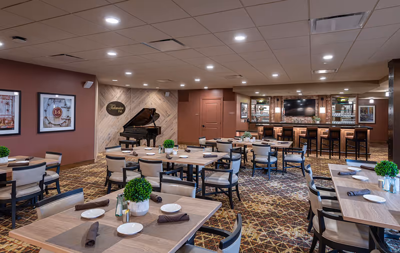 Spacious dining room with multiple set tables, a bar area, and a grand piano.