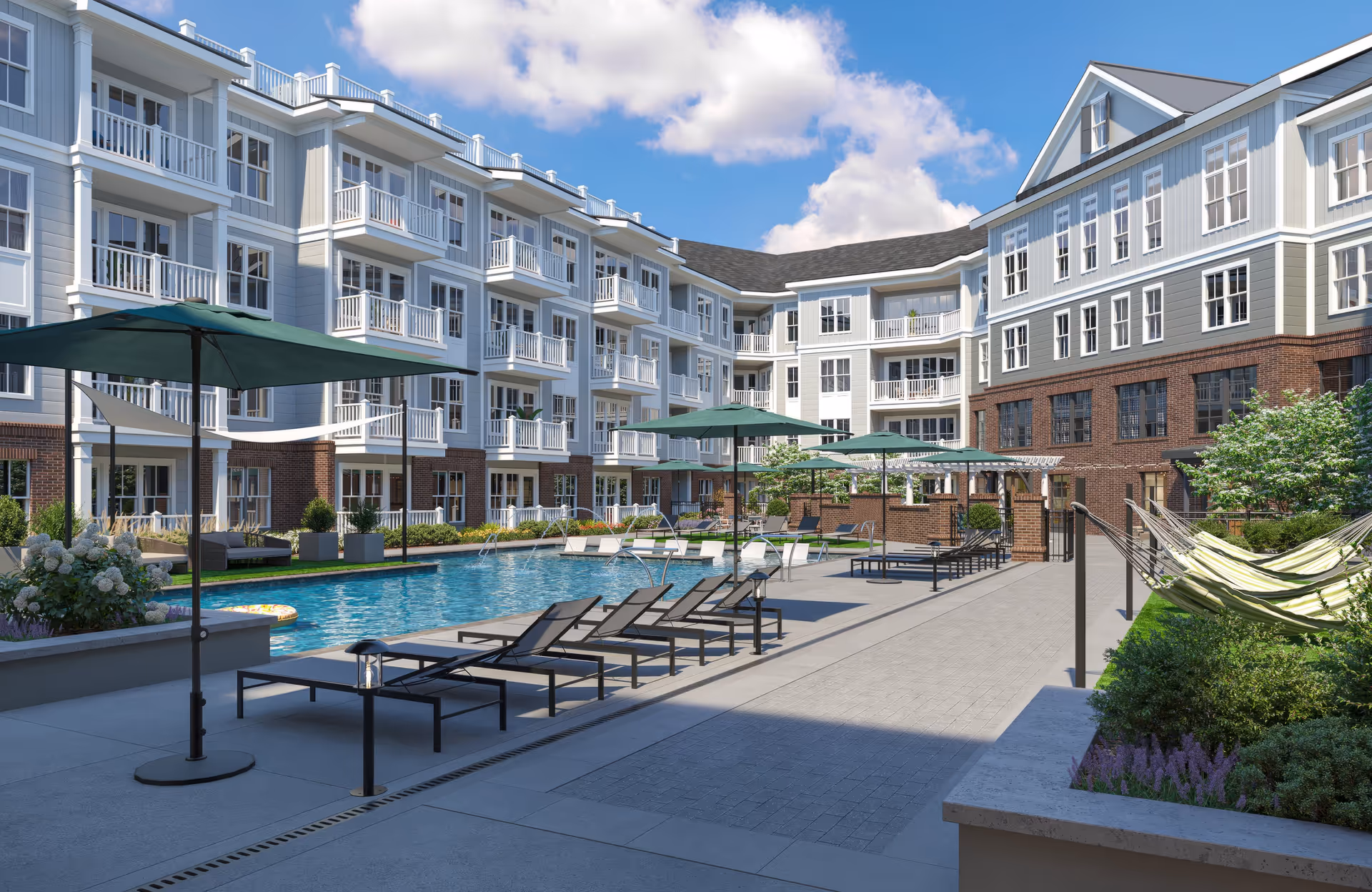 Outdoor courtyard area of a senior living facility featuring a swimming pool surrounded by lounge chairs and umbrellas. The multi-story building with balconies and large windows encloses the pool area. There are also hammocks and landscaped greenery around the pool deck under a partly cloudy blue sky.