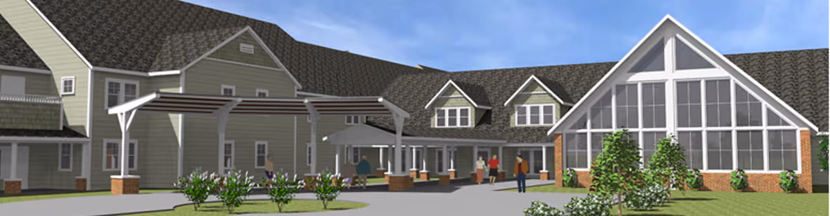 Exterior view of a senior living facility with green siding and multiple peaked roofs. The building features large windows, a covered entrance with a pergola, and landscaped greenery with bushes and grass in front. Several people are walking near the entrance.