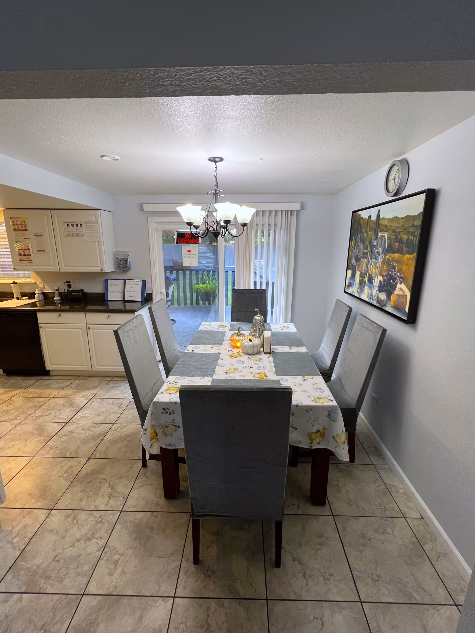 Dining room with a rectangular table set for six, upholstered chairs, a chandelier overhead, and sliding glass doors to an outdoor area.