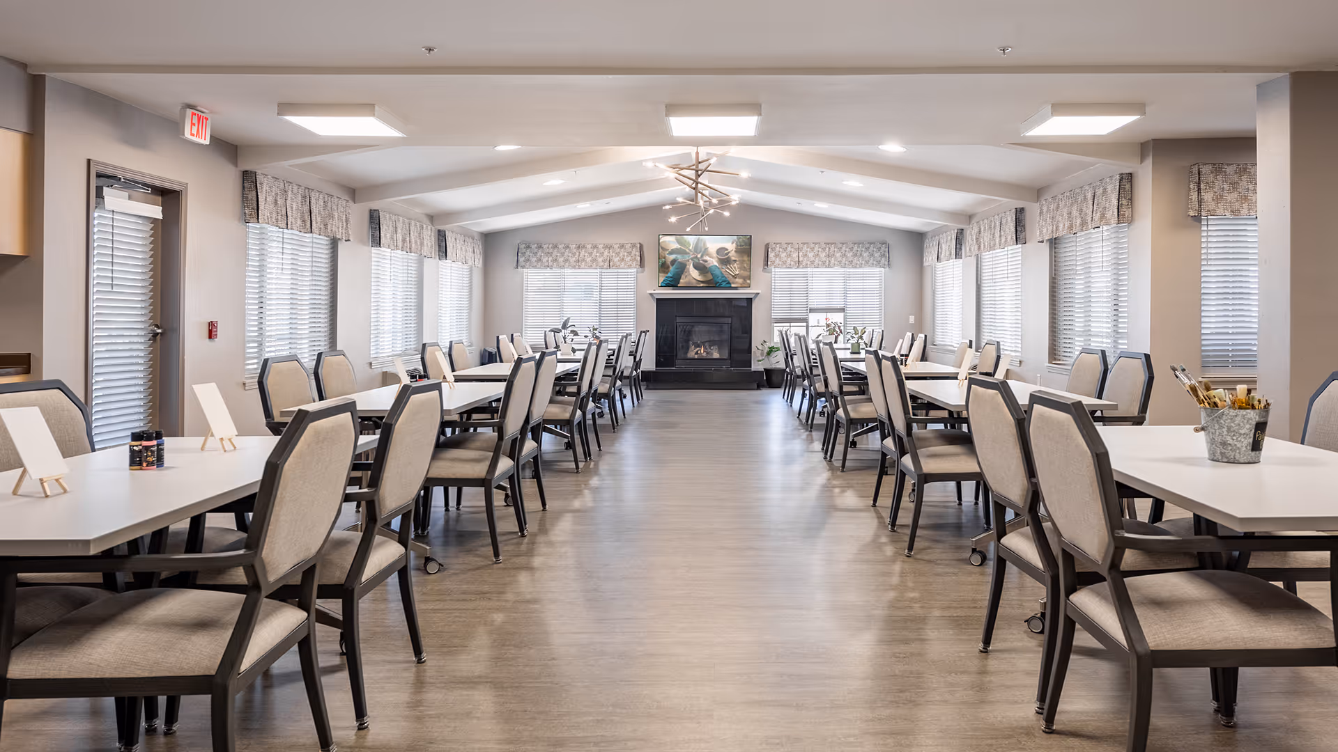 Spacious communal dining room with rows of tables and chairs and a fireplace at the far end.