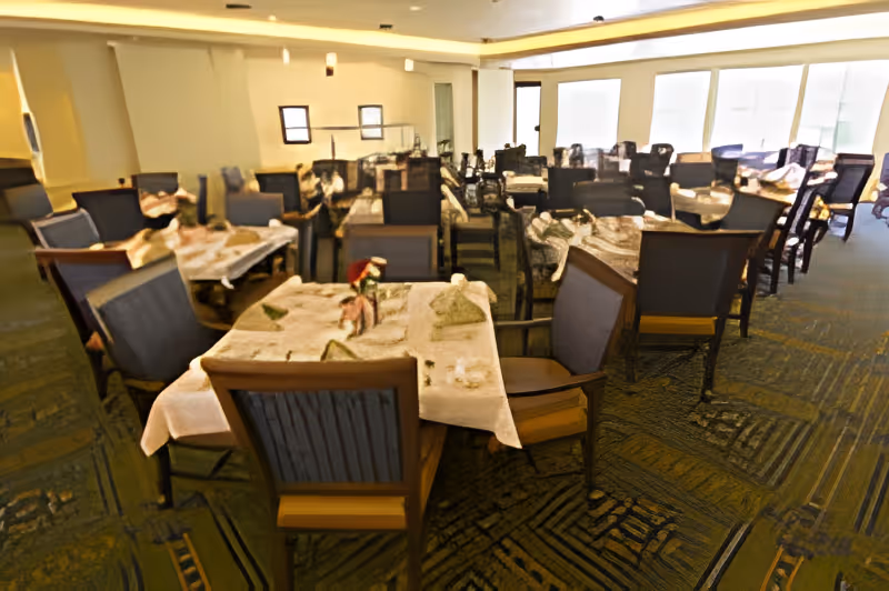 Large dining room with multiple tables set with tablecloths and chairs.