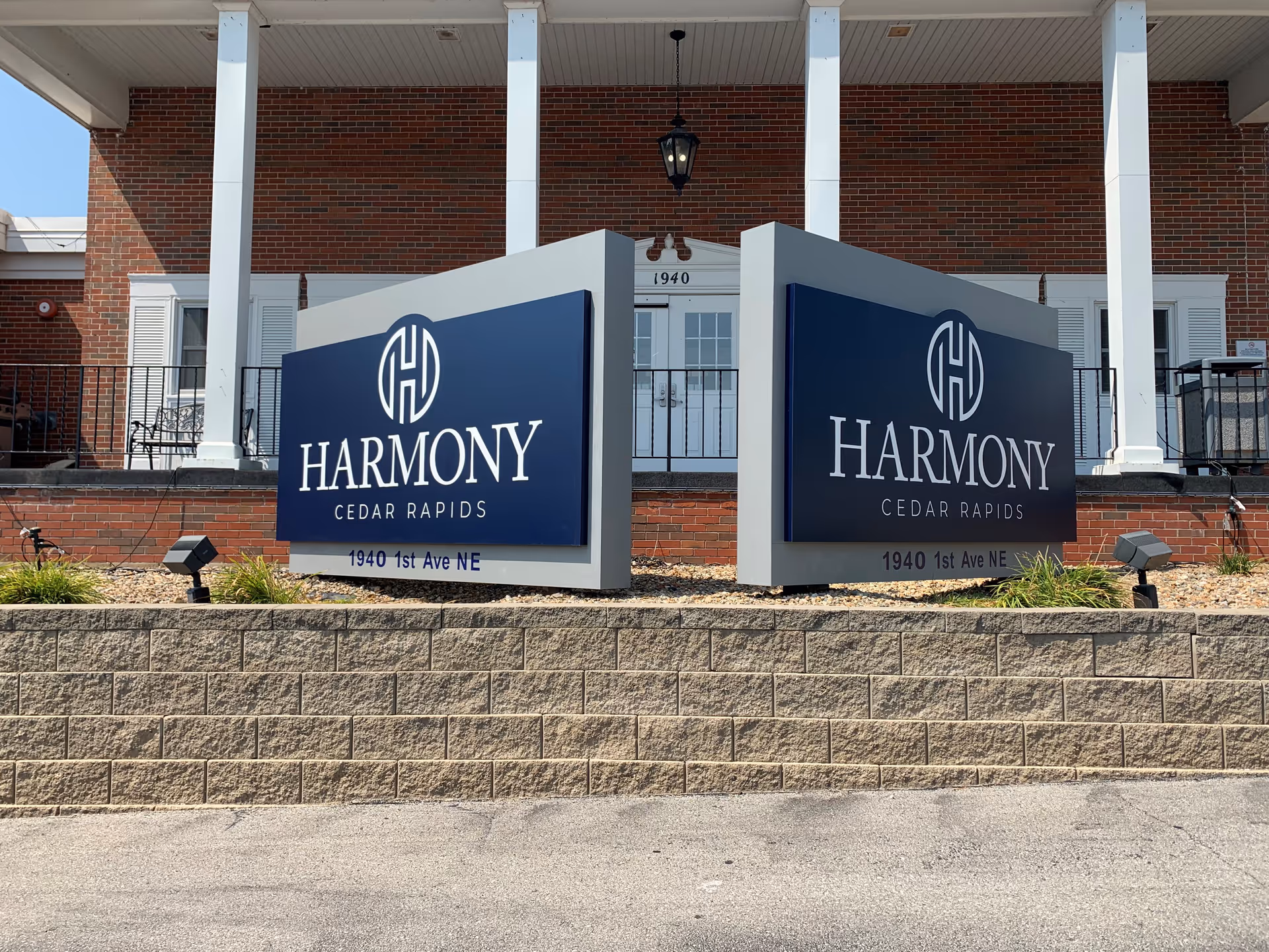 Front of a brick building with two large blue signs reading "Harmony Cedar Rapids" and the address in front of a porch entrance.