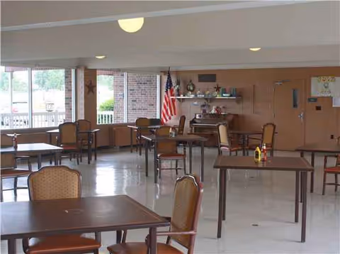 Interior dining room with empty tables and chairs, flag, piano, and shelves.