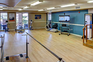 Bright senior exercise room at Marquis Care Plaza Regency with treadmills, bikes, and parallel bars.