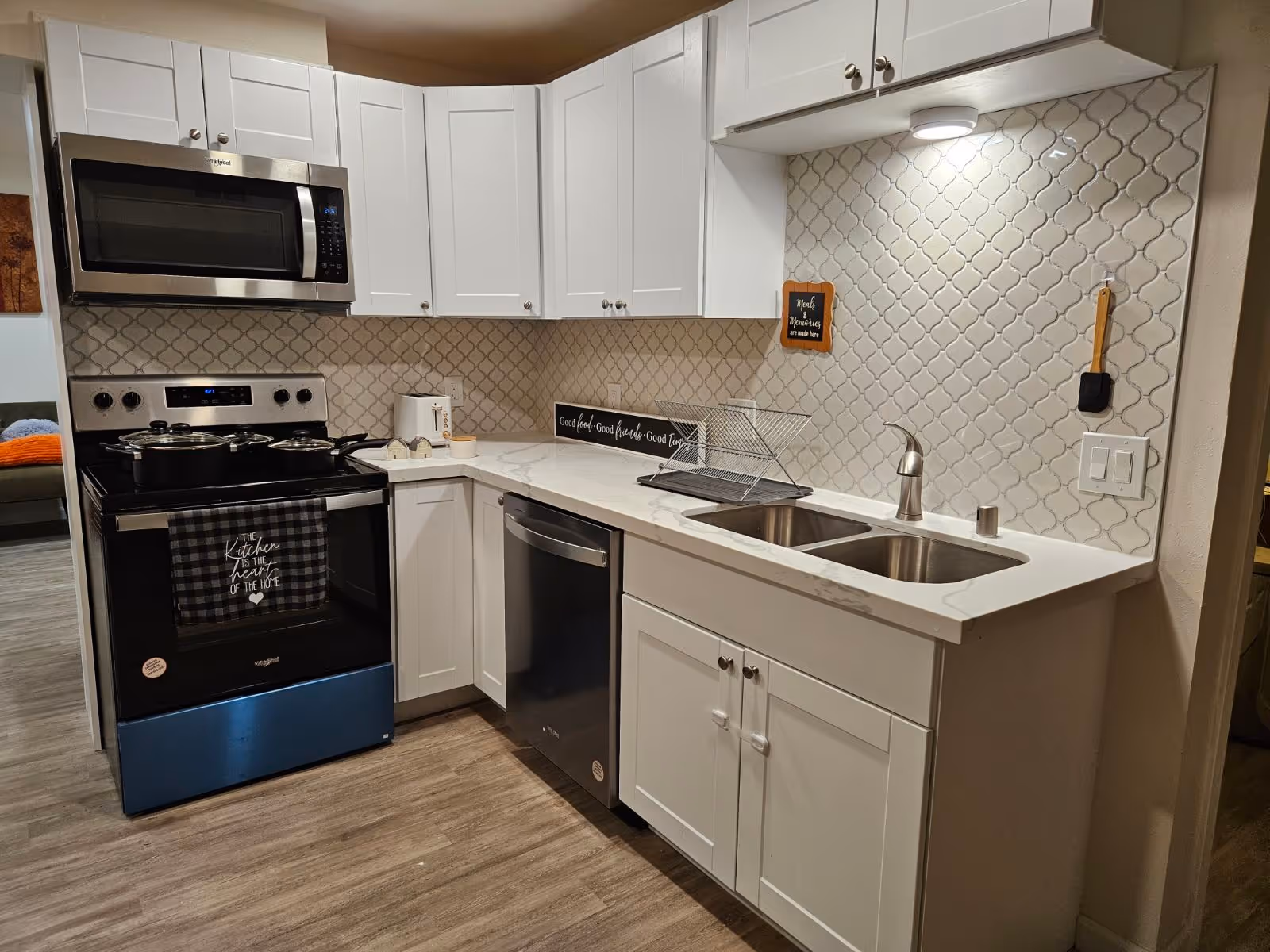 Modern white kitchen with stainless steel appliances, double sink, white cabinets and patterned tile backsplash.