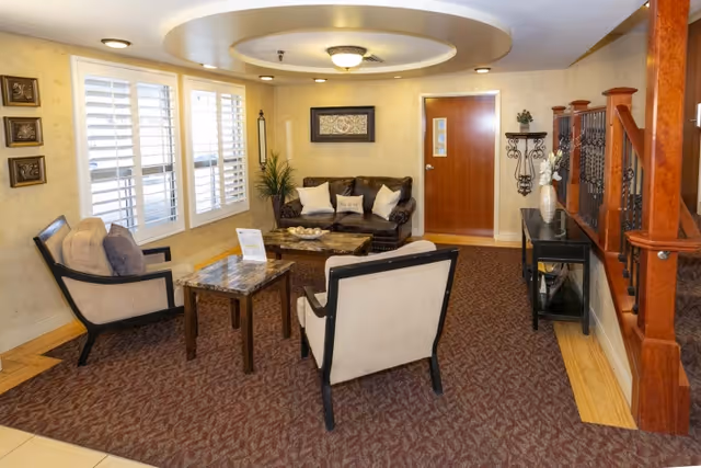 Cozy interior sitting area with chairs and a sofa arranged around a coffee table under decorative ceiling lighting.