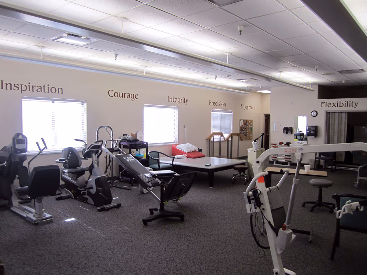 Rehabilitation/exercise room with cardio equipment, therapy tables, and motivational words on the walls.