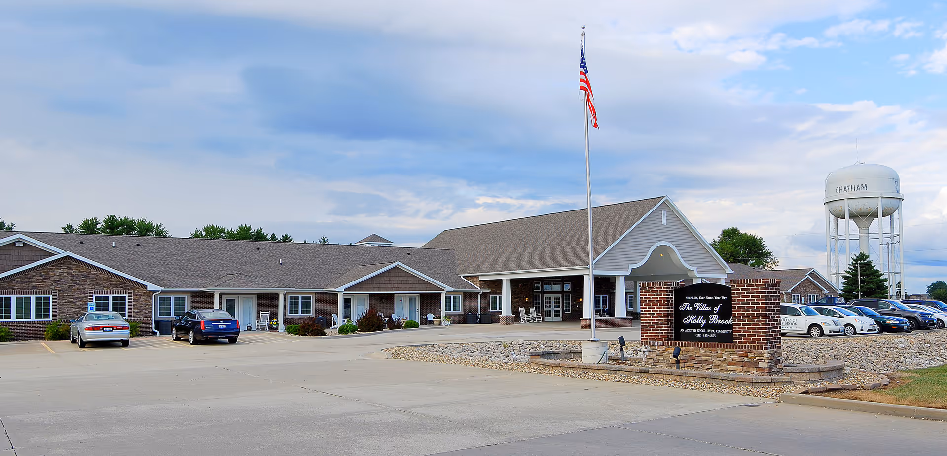 Single-story senior living facility with flagpole, parking, and a water tower in background.