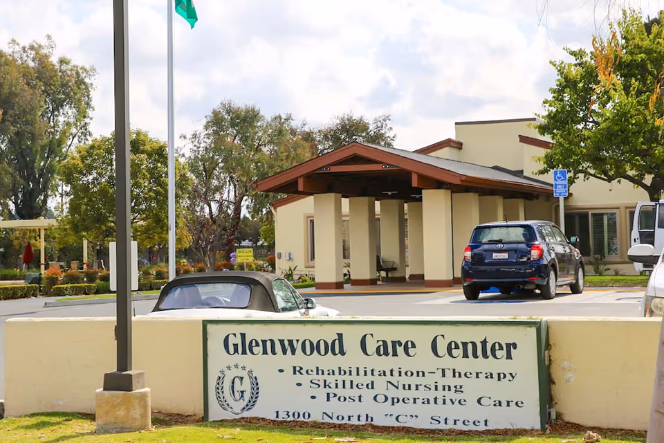 Entrance to Glenwood Care Center with a sign in the foreground, a covered porte-cochere, and parked cars.