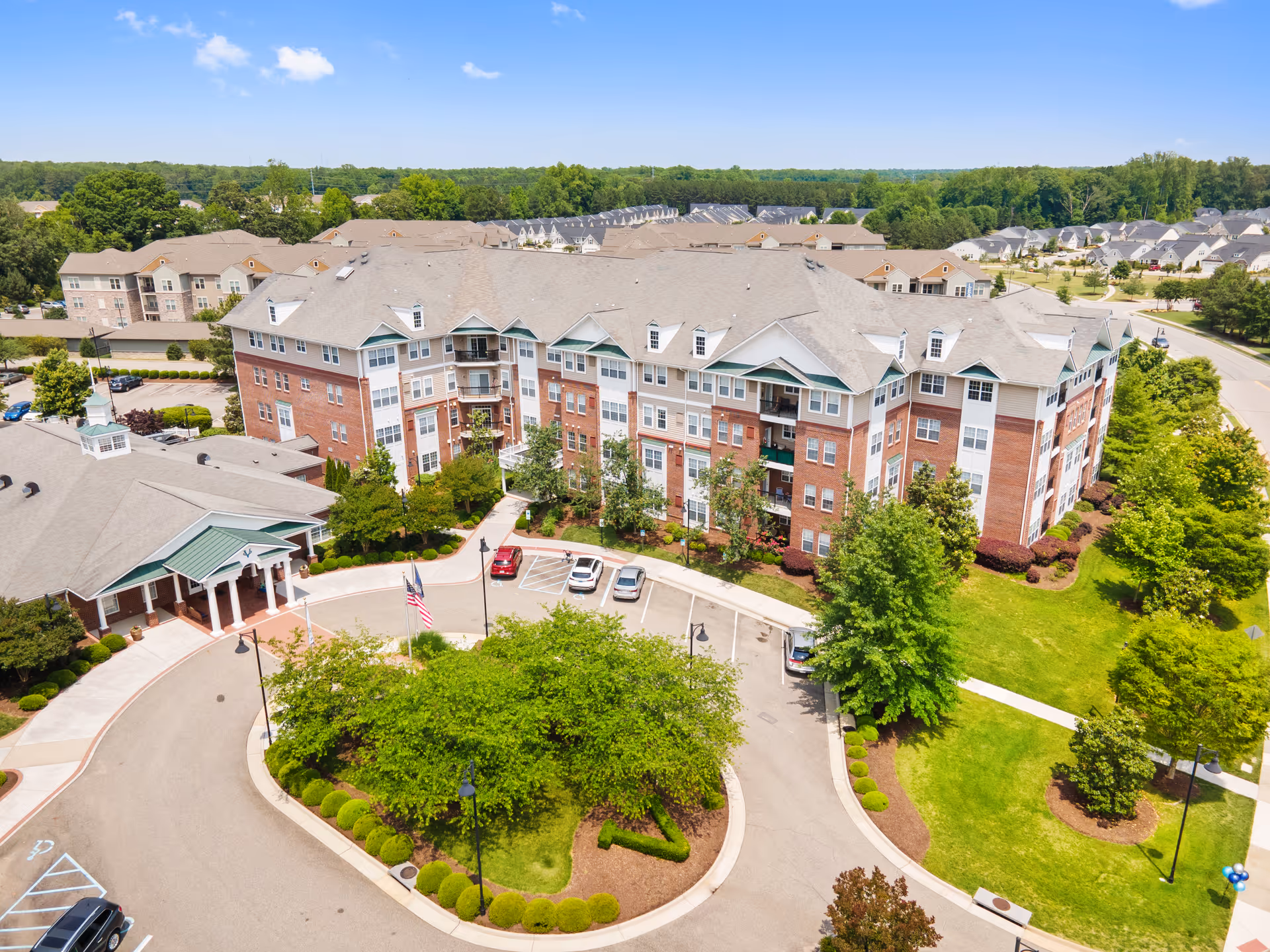 Aerial view of a multi-story senior living building with a landscaped circular drive, entrance canopy, and parking area.
