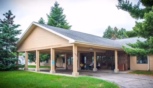 Front exterior of a senior living building with a covered entrance canopy, drive-up area, and surrounding trees.