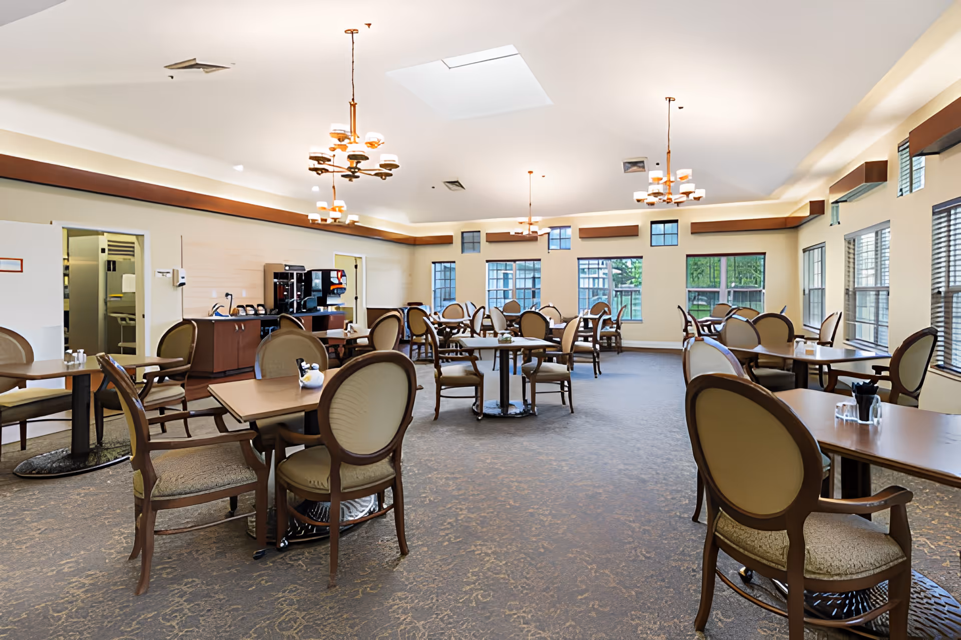 Bright, spacious dining room with multiple tables and upholstered chairs, chandeliers, and large windows.