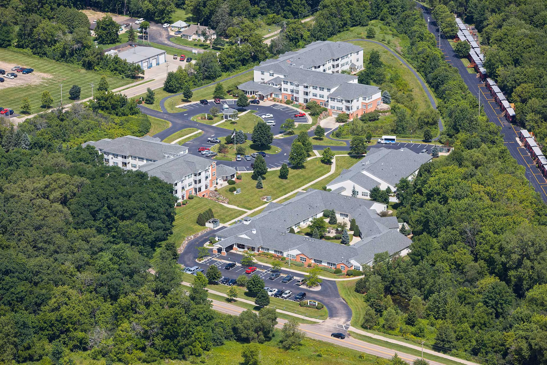 Aerial view of the Highlands of Geneva Crossing campus showing multiple connected residential buildings, parking areas, driveways, and surrounding trees.