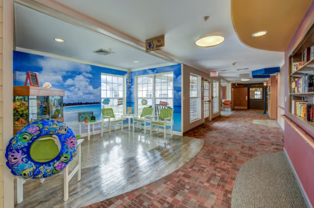 Bright interior hallway with a beach-themed seating nook featuring green chairs, a large beach mural, an aquarium and bookshelves.