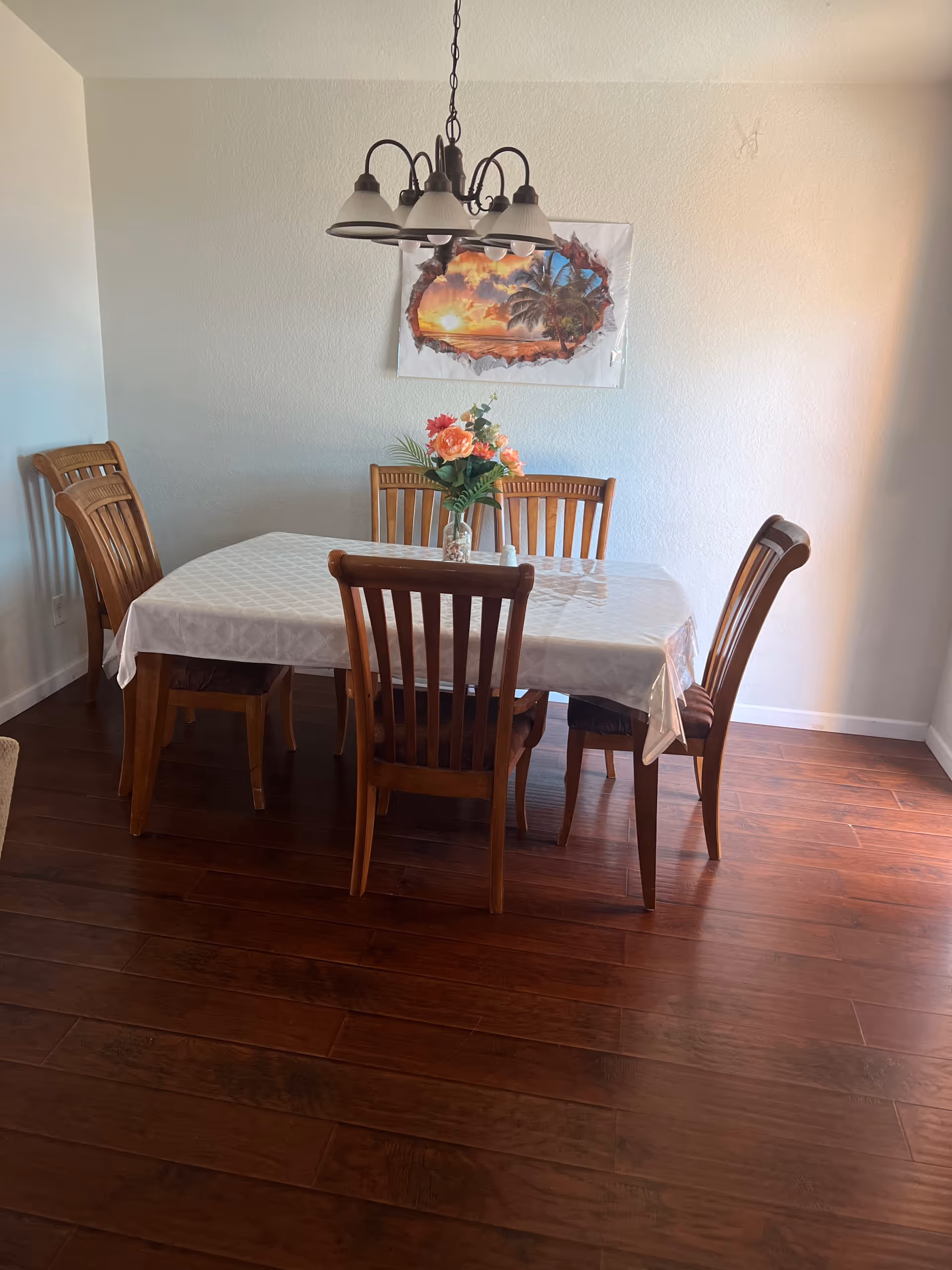 Wooden dining table with six chairs, a vase of flowers, a hanging light fixture, and wall art in a dining room.