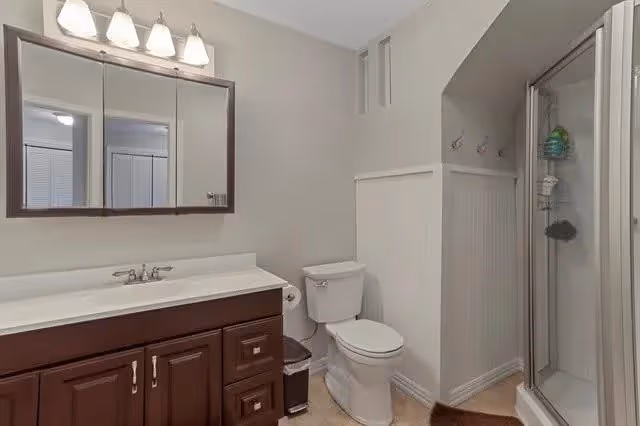 Clean bathroom with a dark wood vanity and mirrored cabinet, toilet, and glass corner shower.