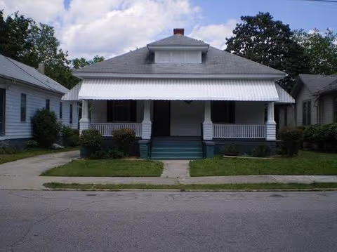 Front view of a small white house with a covered porch and awning.