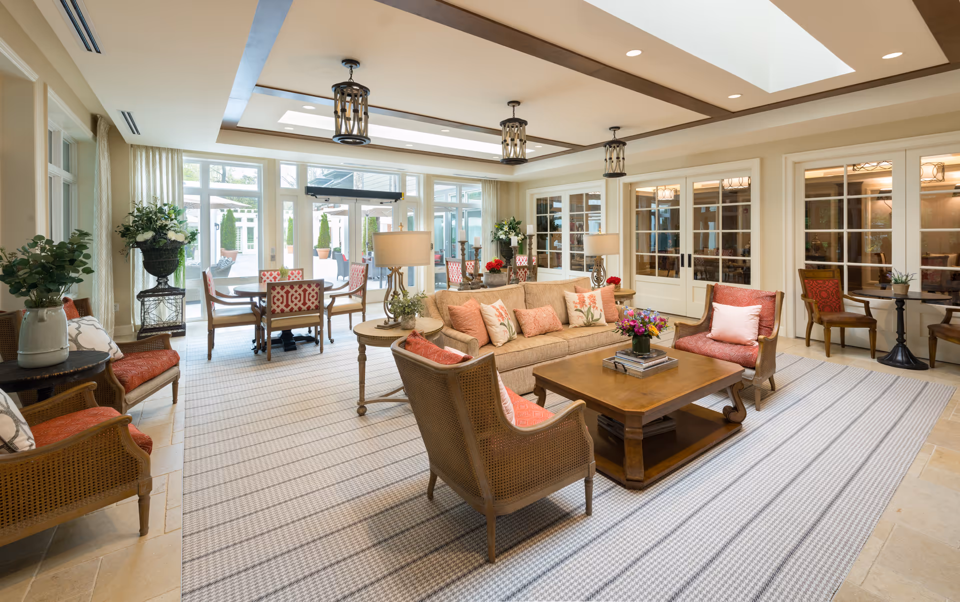 Bright, open communal living room with a sofa, armchairs, coffee table, and dining area opening to an outdoor patio.
