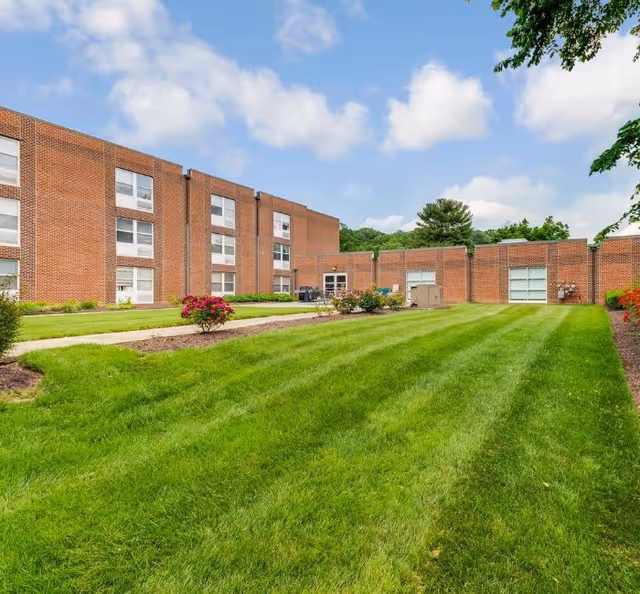 A well-maintained green lawn with neatly trimmed grass and flower beds in front of a multi-story brick building under a partly cloudy sky.