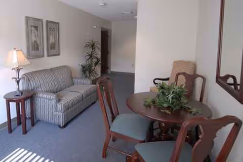 Cozy senior living common area with striped sofa, lamp, framed art, and round dining table.