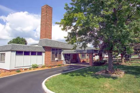 Exterior view of The Lane House senior living facility with a curved driveway and trees.