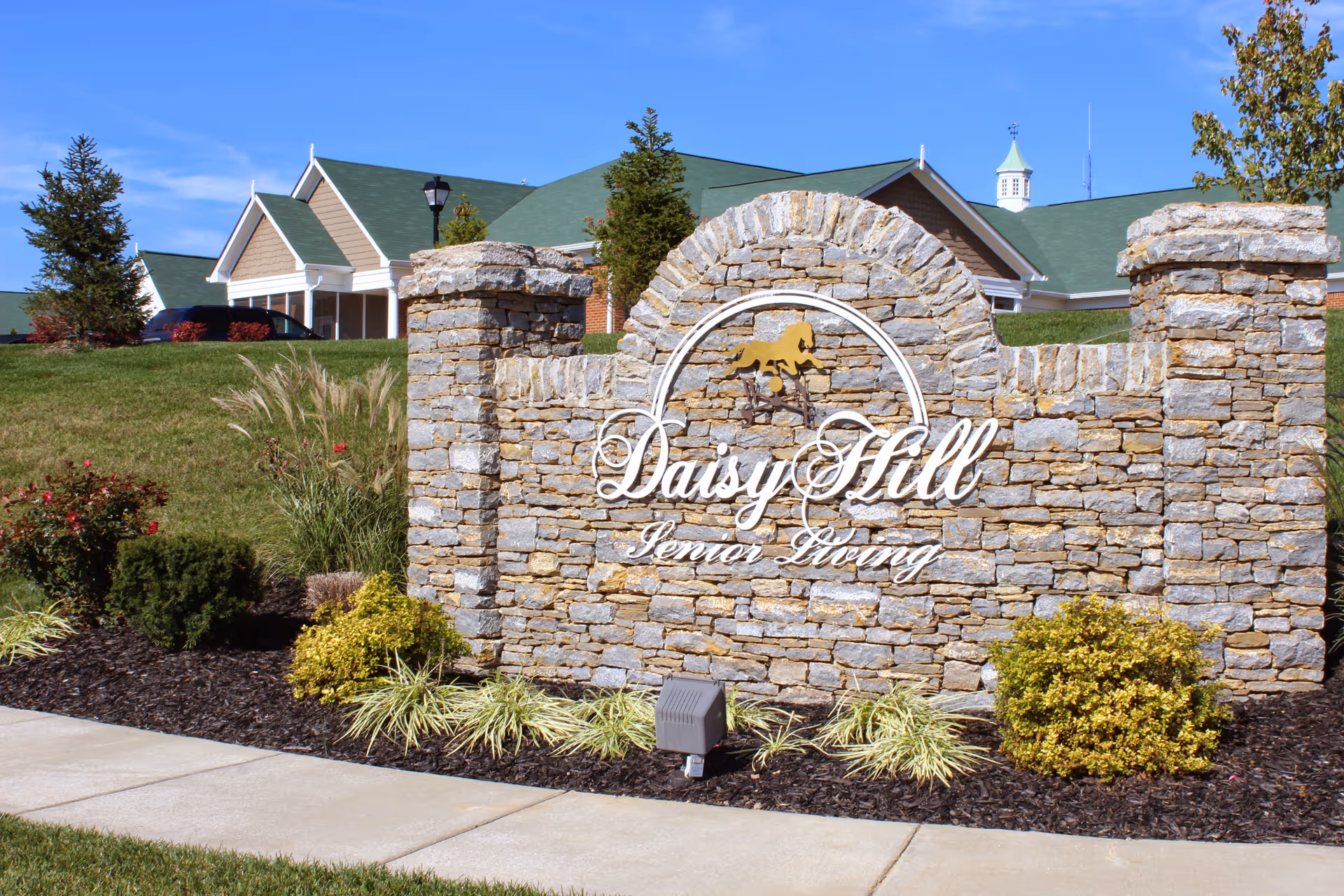 Stone entrance sign reading "Daisy Hill Senior Living" surrounded by landscaping with the facility buildings in the background.