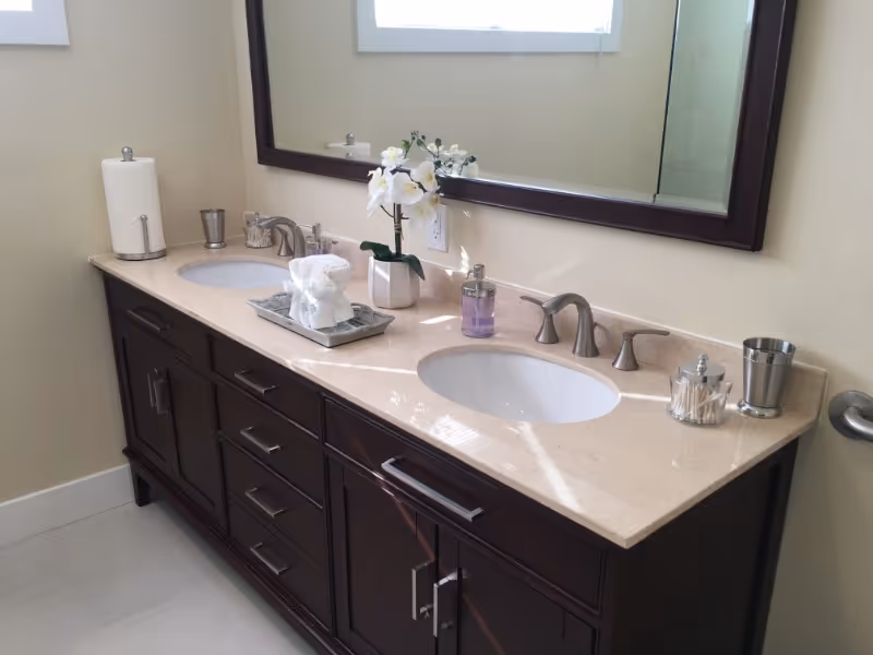 Double-sink bathroom vanity with a marble countertop, dark wood cabinets, large mirror and a decorative orchid.