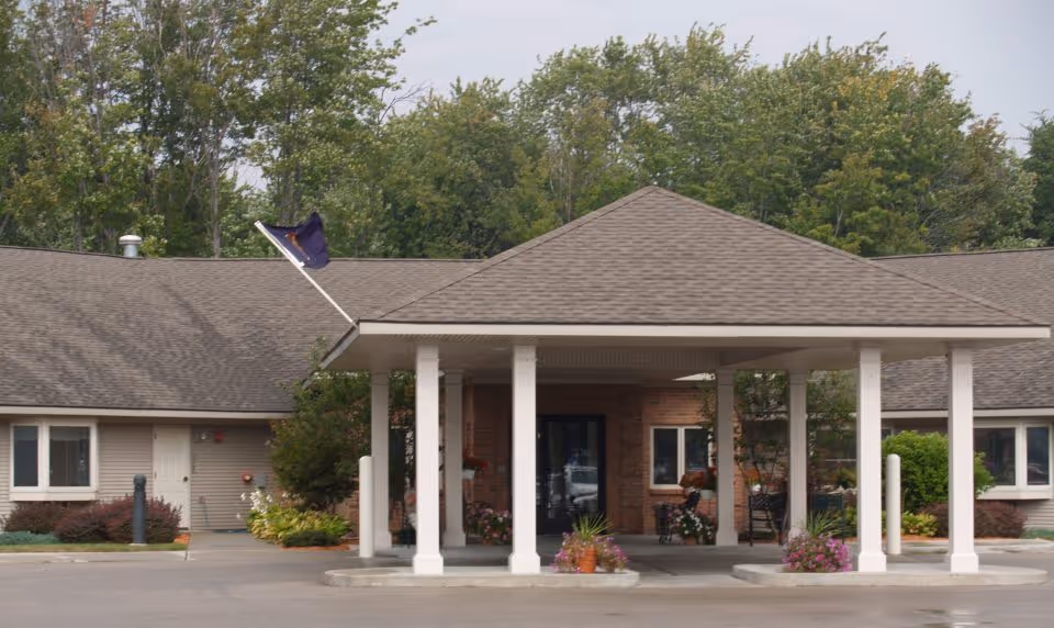 Front exterior view of Seminole Shores Living Center showing a covered entrance with white pillars, a driveway, and surrounding greenery including trees and shrubs.