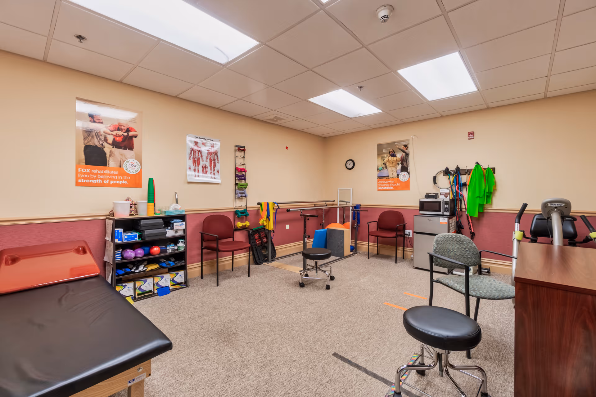 A physical therapy room with exercise equipment, chairs, and instructional posters on the walls.