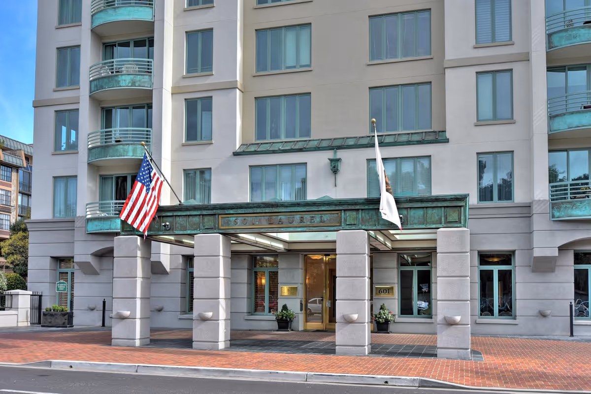 Front entrance of a multi-story residential building with a covered porte-cochère, an American flag, and balconies.